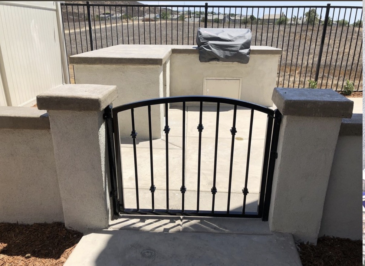 Black iron arched garden gate between stucco columns