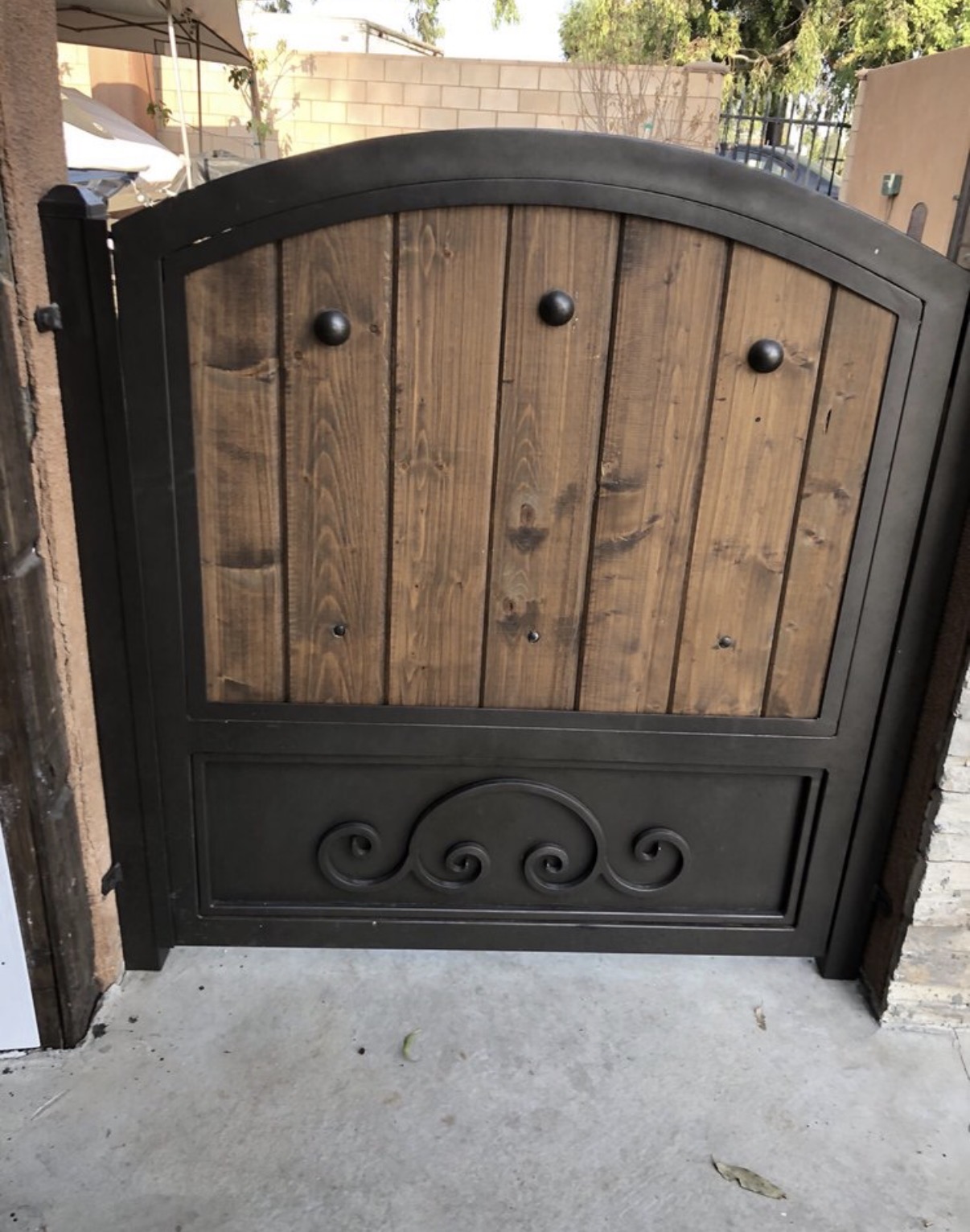 Arched wood and iron side gate with scrollwork base panel