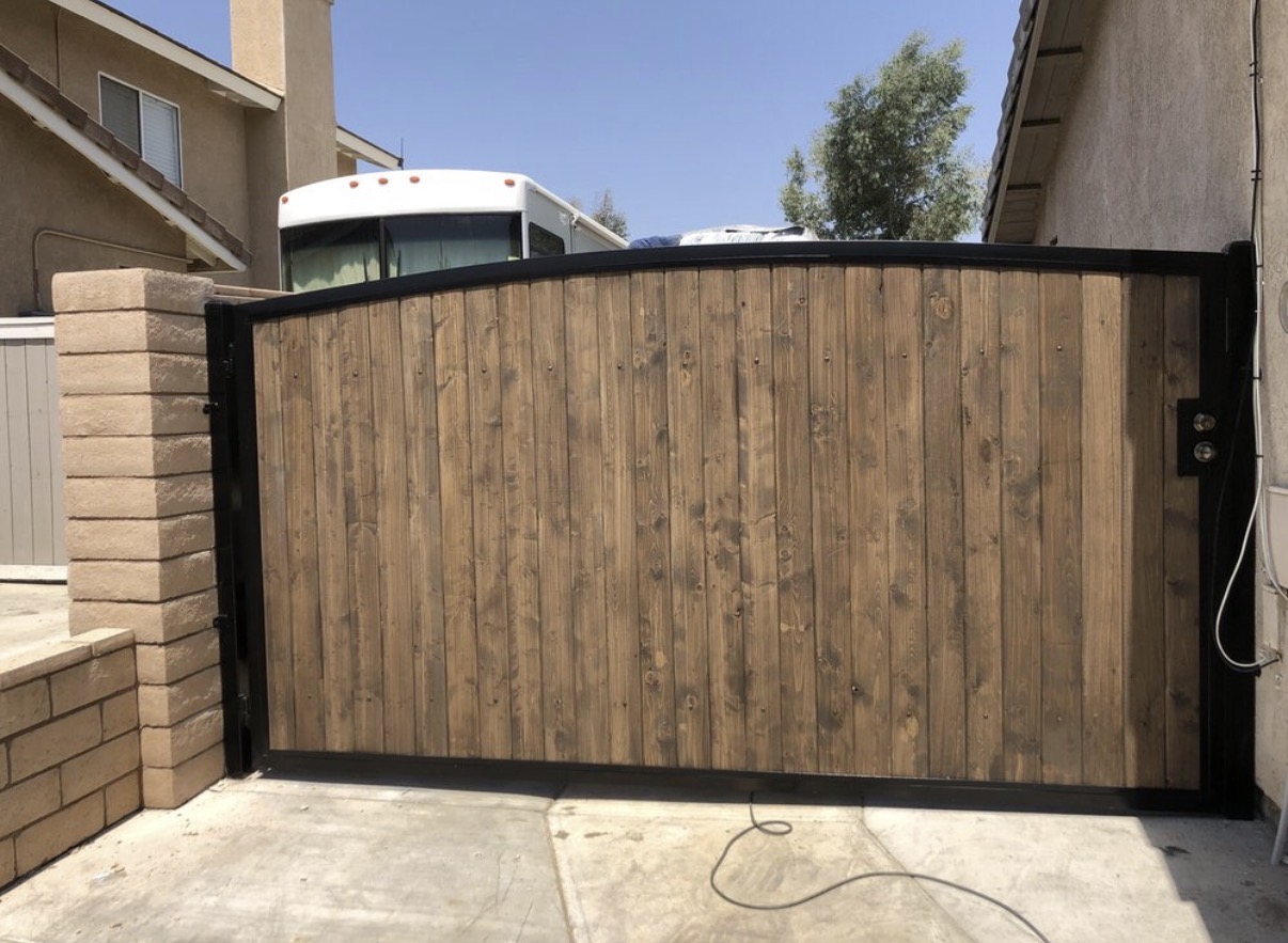 Arched wood driveway gate with iron frame between stucco columns