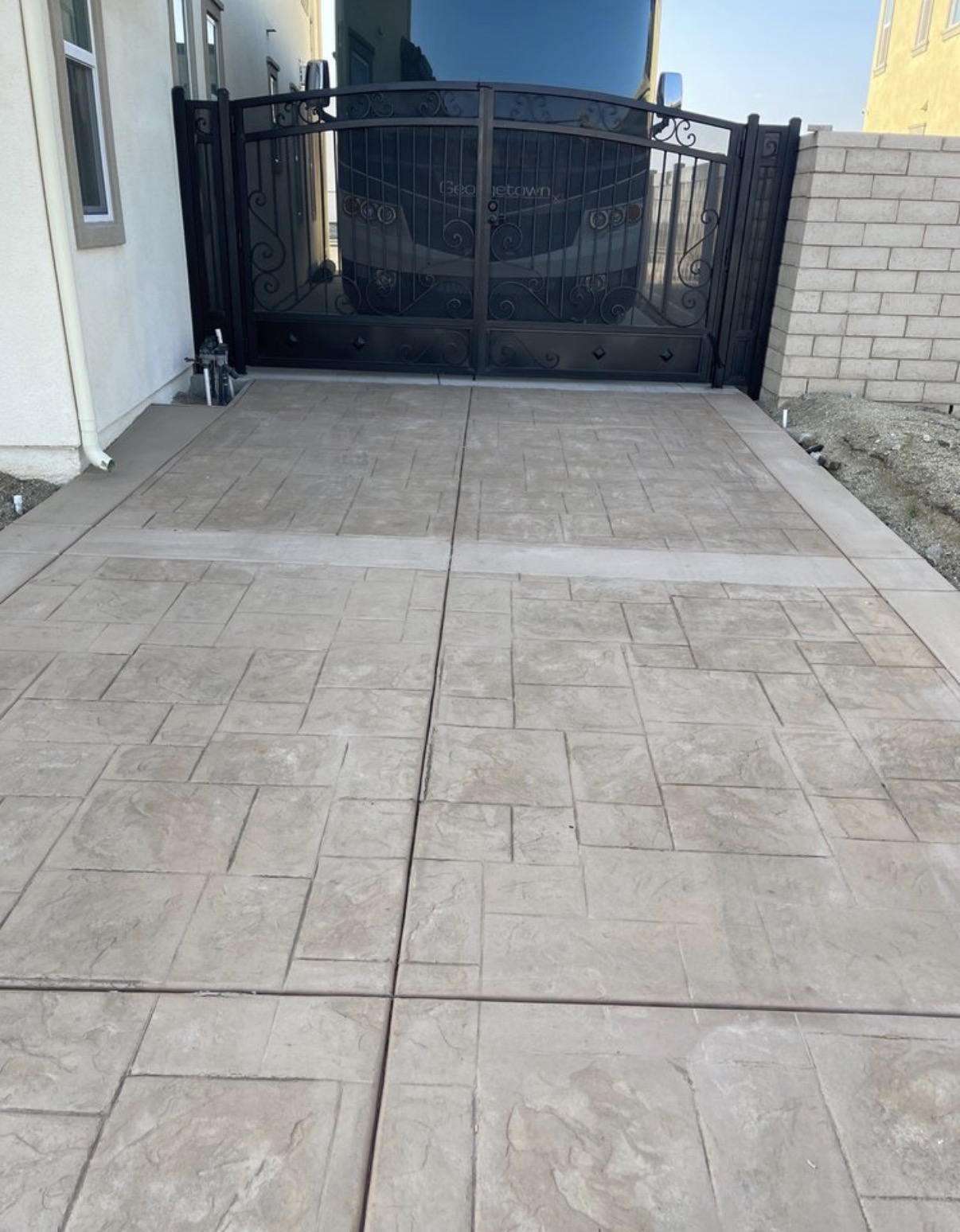 Black iron driveway gate with scrollwork over stamped concrete