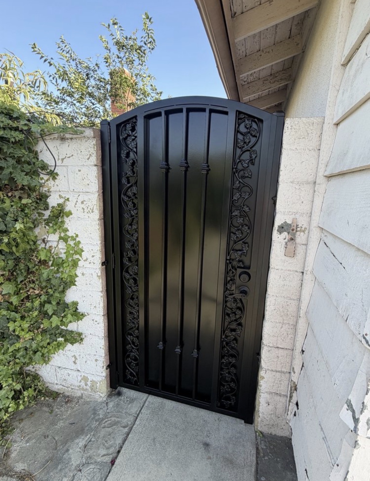 Black iron arched side gate with grape vine scrollwork panels